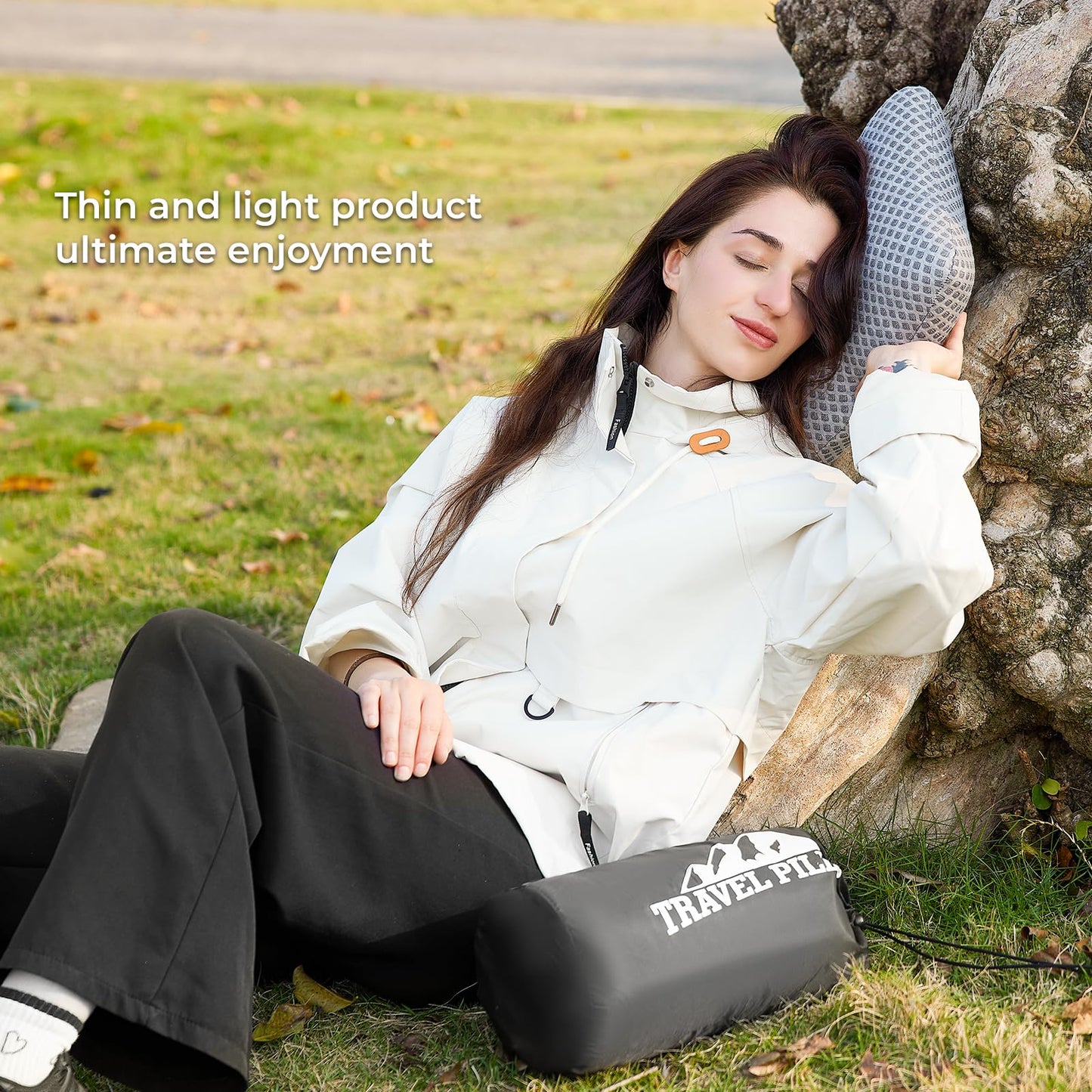 Woman resting outdoors against a tree using a Memory Foam Travel Pillow for Ultimate Comfort on the Go, with a compact travel pillow bag nearby on the grass.